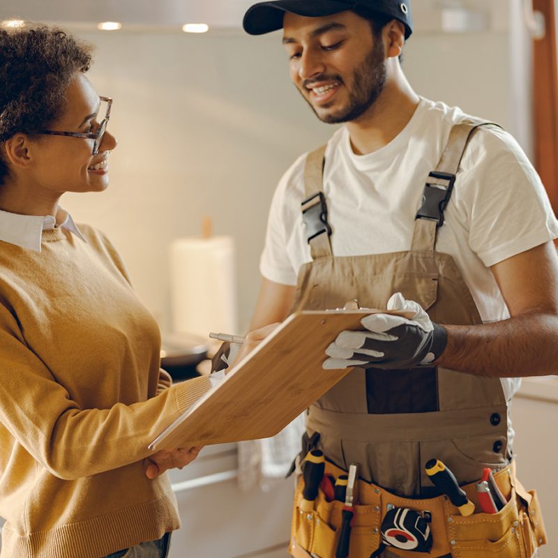 Smilng young woman signing document while communicating with handyman at the kitchen